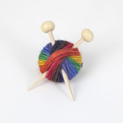 A brooch made with rainbow yarn and 2 wooden knitting needles